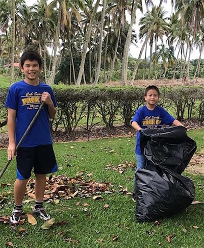 two boys in blue Cub Scout t-shirts bag leaves on a lawn