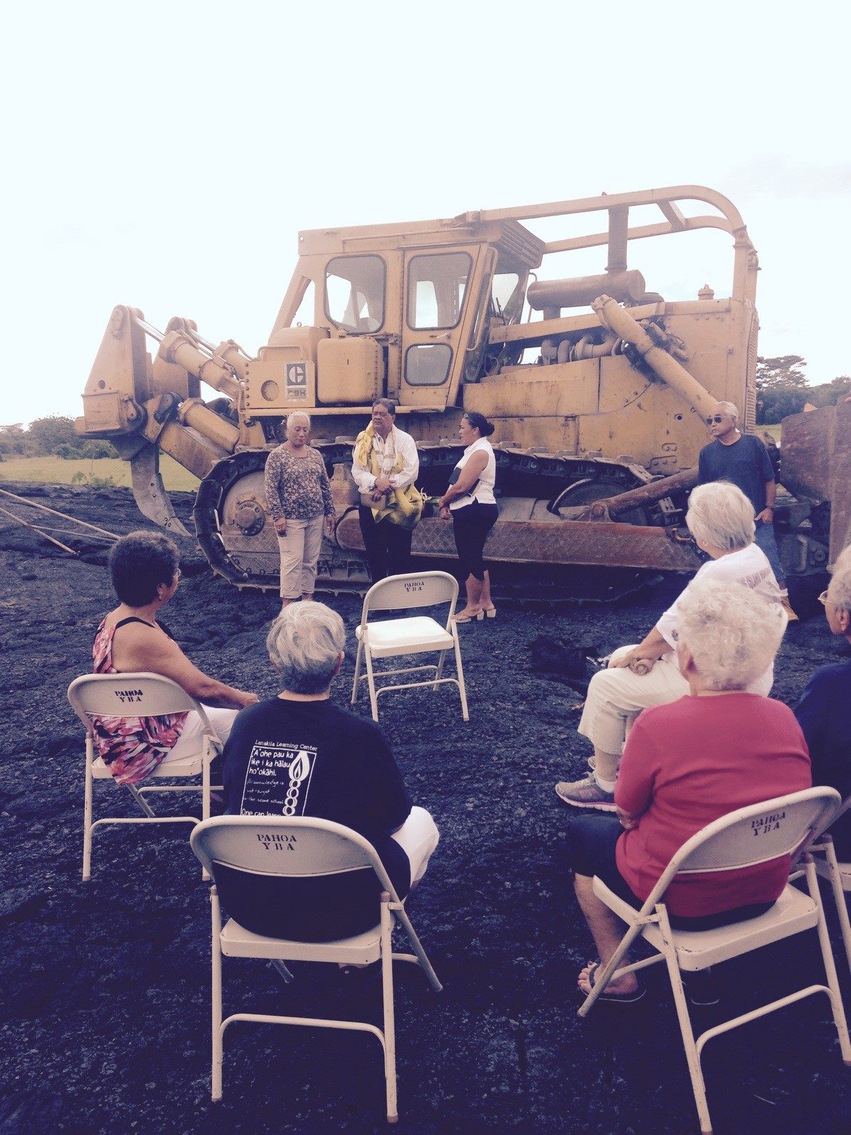 people seated in folding chairs on the lava flow with big earth moving equipment in the background