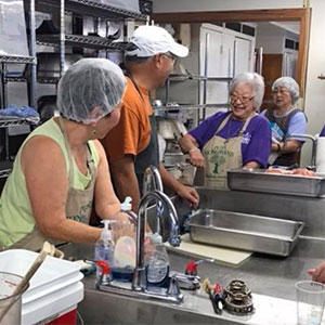 volunteers with headnets and hats smiling in the kitchen
